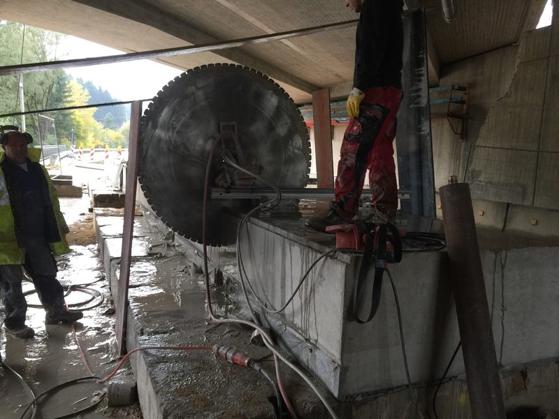 Übergroßes Wandsägeblatt trennt ein massives Betonbauteil; Mitarbeiter im Einsatz